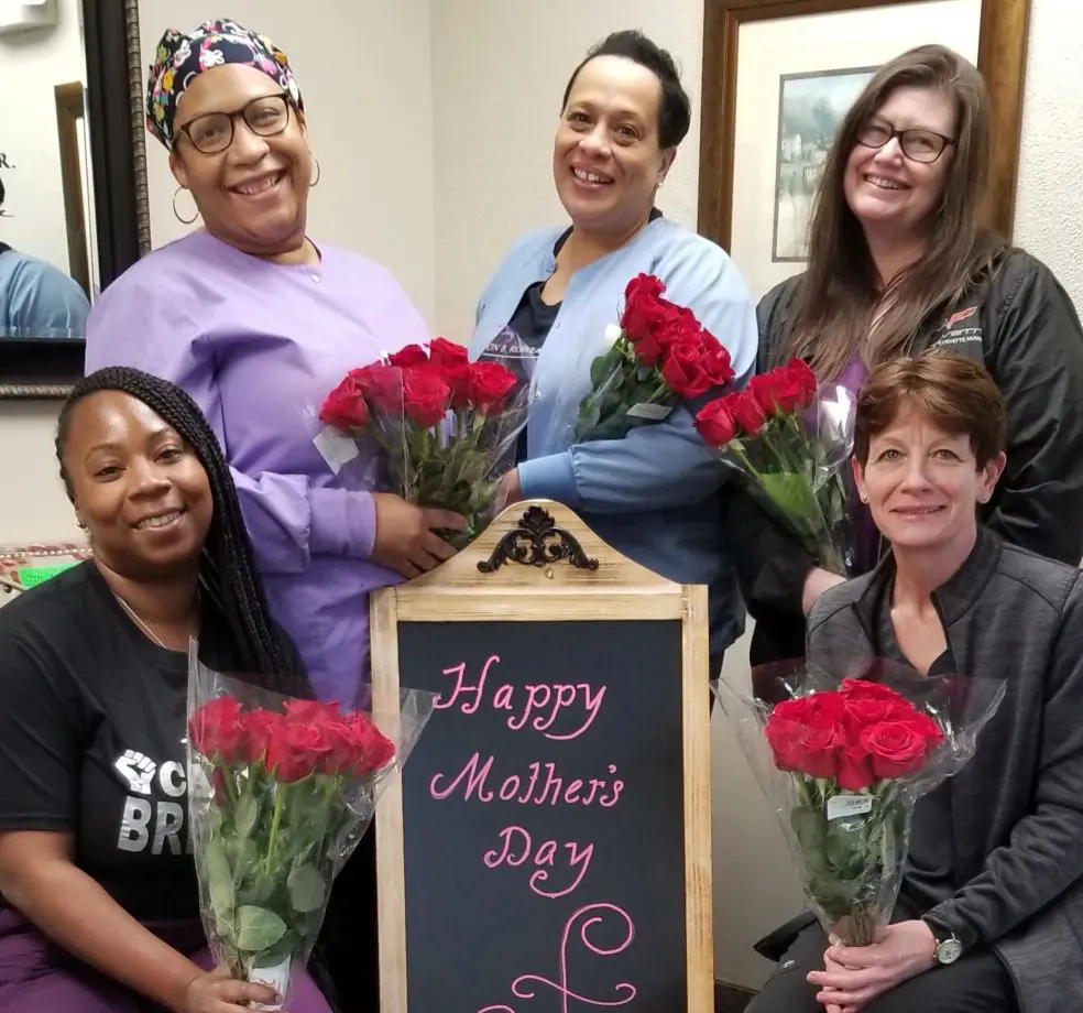 A group of women holding roses in front of a sign.